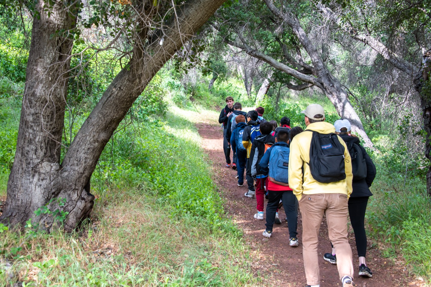 Students hiking a shaded trail at Camp Ramah, led by a staff member